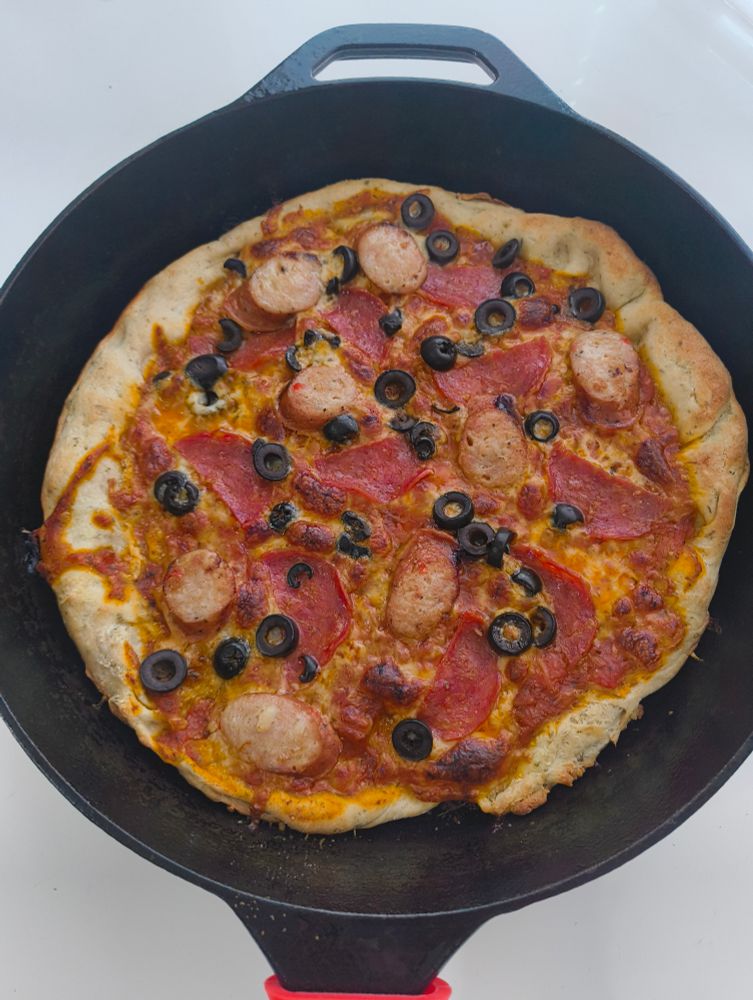 Photo of a pepperoni, olive & sausage pizza resting in a cast iron pan.