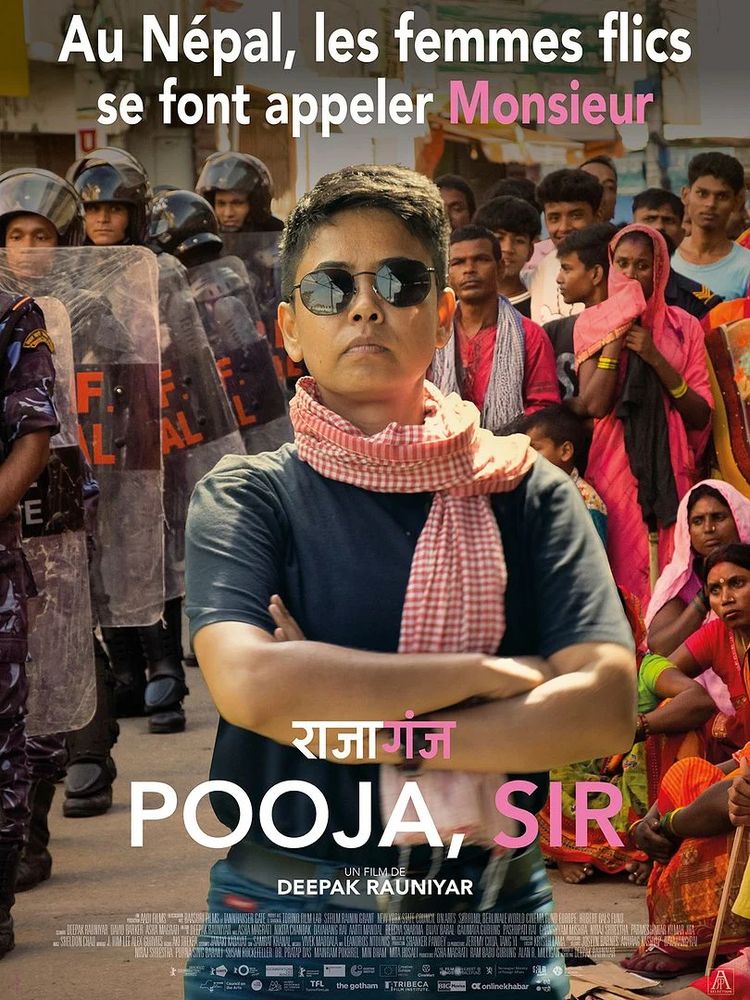 Affiche du film "Pooja, Sir". Accroche en haut: Au Népal, les femmes flics se font appeler Monsieur.
Image: au premier plan, une femme aux cheveux très courts, en T-shirt sombre, un foulard à petits carreaux rouges et blancs enroulé au cou, portant des lunettes noires, nous regarde en face, les bras croisés, l'air déterminé. Derrière, à gauche un groupe de policiers anti-émeutes, avec boucliers transparents et casques, à droite, des civils en tenues traditionnelles, hommes et femmes