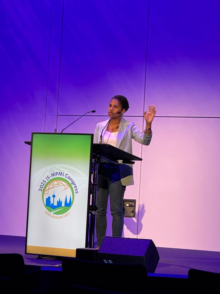 A woman giving a talk at a lectern with an MPMI logo