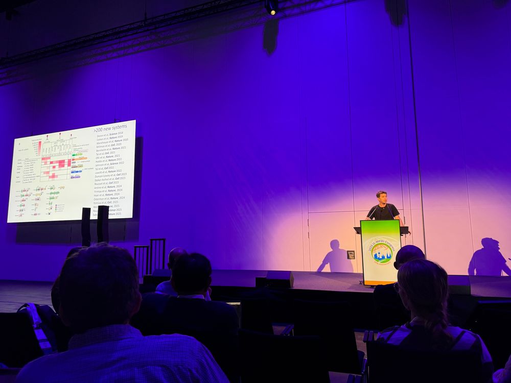 A large conference stage with a man presenting with a power point slide showing a scientific figure about bacterial immunity