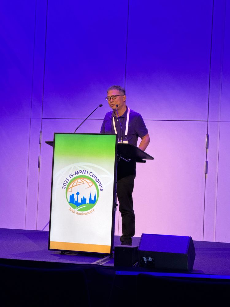 A man speaking at a lectern with an MPMI logo