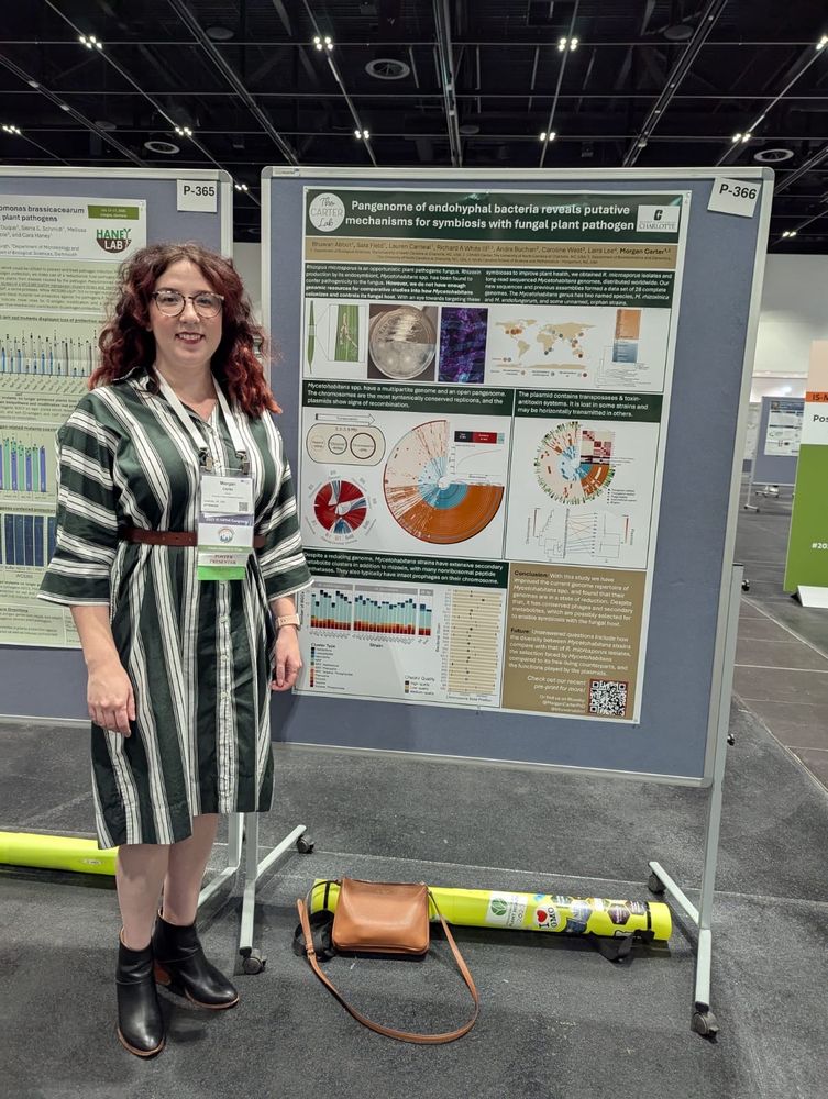 Me, a white woman with fluffy curly hair and  striped dress standing in front of a scientific poster with the figures from the linked preprint 