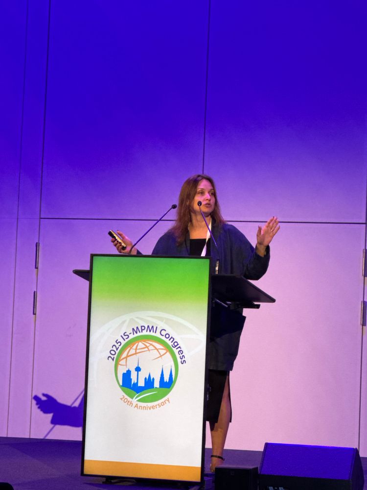A woman talking at a lectern with MPMI logo