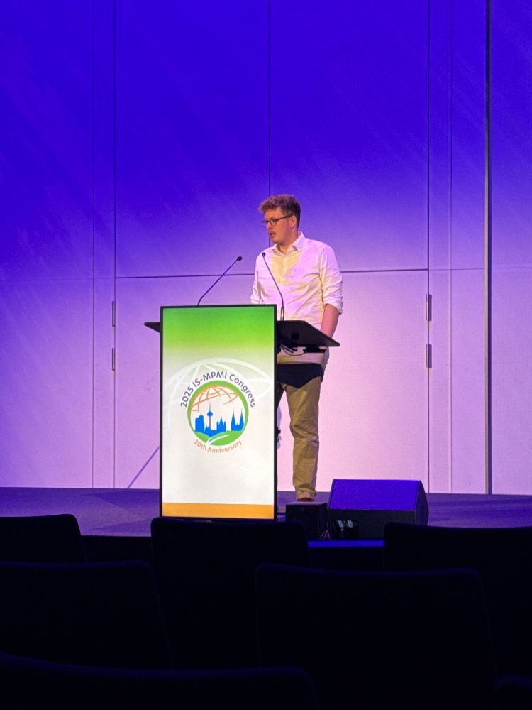 A man giving a presentation at a lectern with an MPMI logo