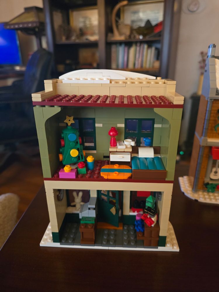 Interior of completed toy store. 1st floor has toy store w/ stuffed bunny & train set in windows, 2nd floor has a bedroom w/ a wish list on the bedside table & a christmas tree with gifts under it