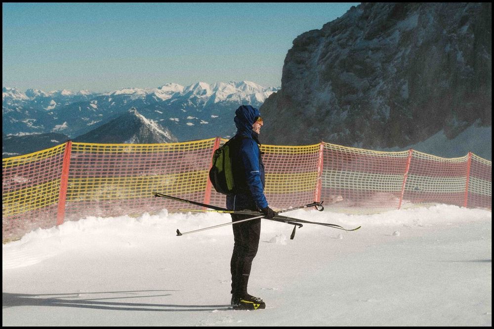 a cross-country skier looking into the distance. Behind him are mountains