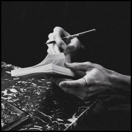 monochrome close up photograph of a man's hand. He is holding a book and a pen