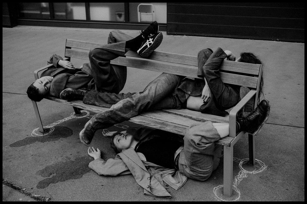 three young people wearing suits using a bench next to the street in unusual ways 