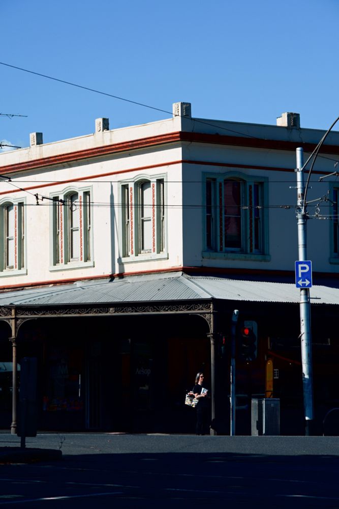 A person stands in shadow beneath a building awning at an intersection 