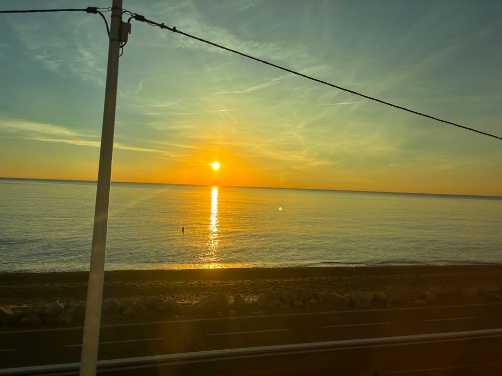 The sun rising over the sea, an empty beach is also visible. 