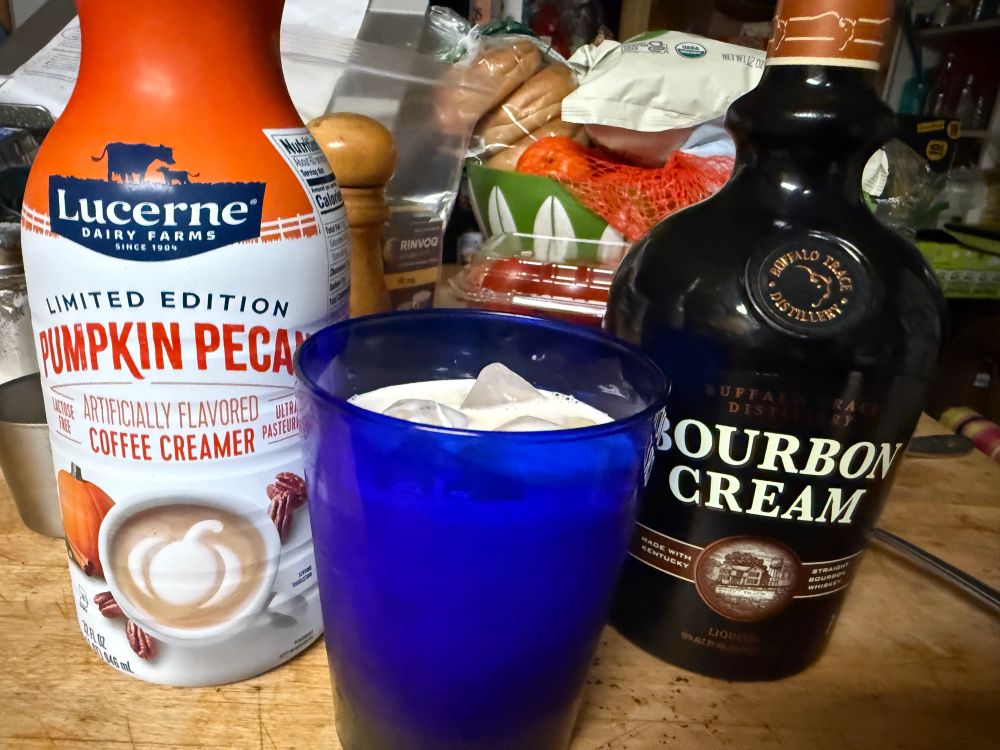 A bottle of pumpkin pecan creamer, a bottle of bourbon cream, a glass containing both and some ice 