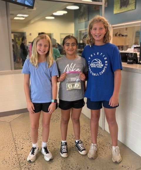 Three young entrepreneurs smile at the camera holding a bag of money they raised at their lemonade stand. 