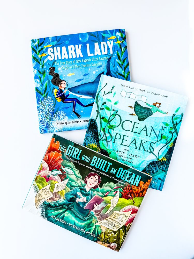 Overhead view of three books - Shark Lady, Ocean Speaks, and the Girl Who Built an Ocean, featuring beautiful blue-toned, colourful covers, and the titular woman on each.