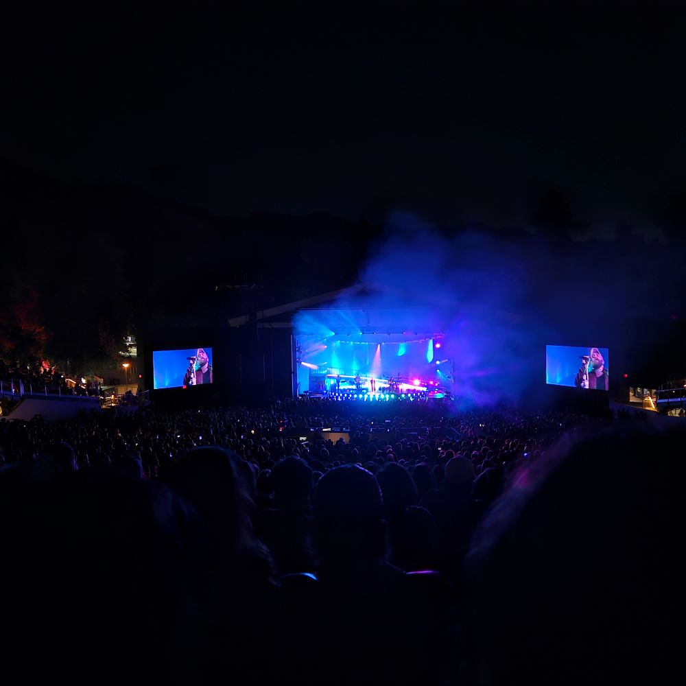 Greek Theater stage, lit blue and pink with a close up of Teddy Swims performing on the screens at either side of the stage