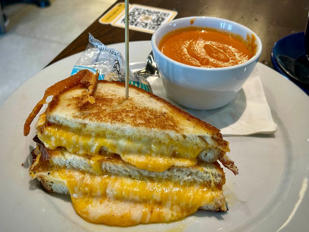 A grilled cheese sandwich overflowing with cheese, and a small cup of tomato soup.