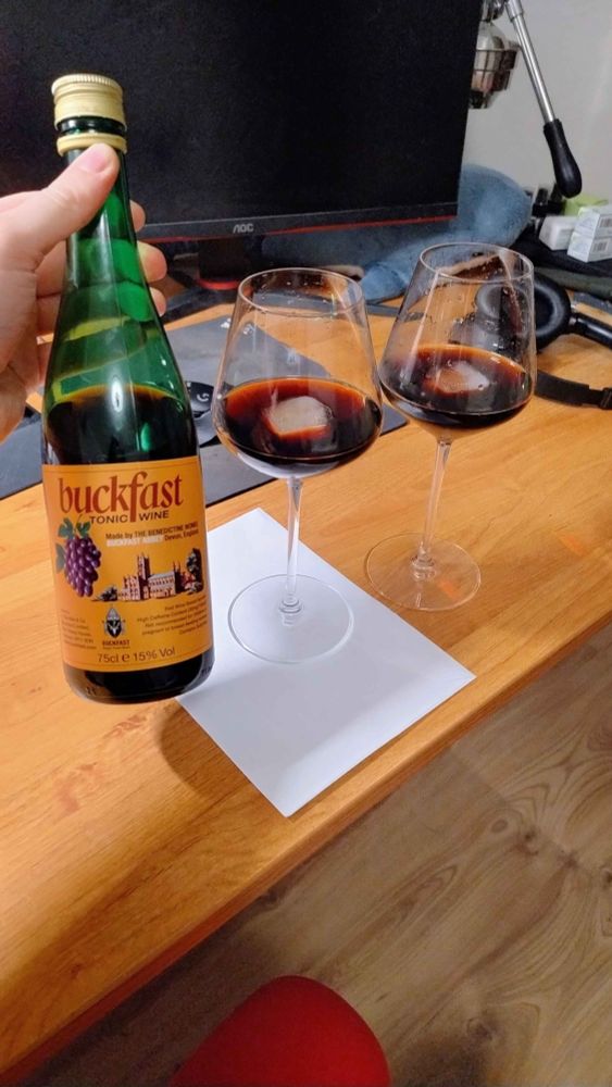 A bottle of buckfast, its contents served over ice in red wine glasses
