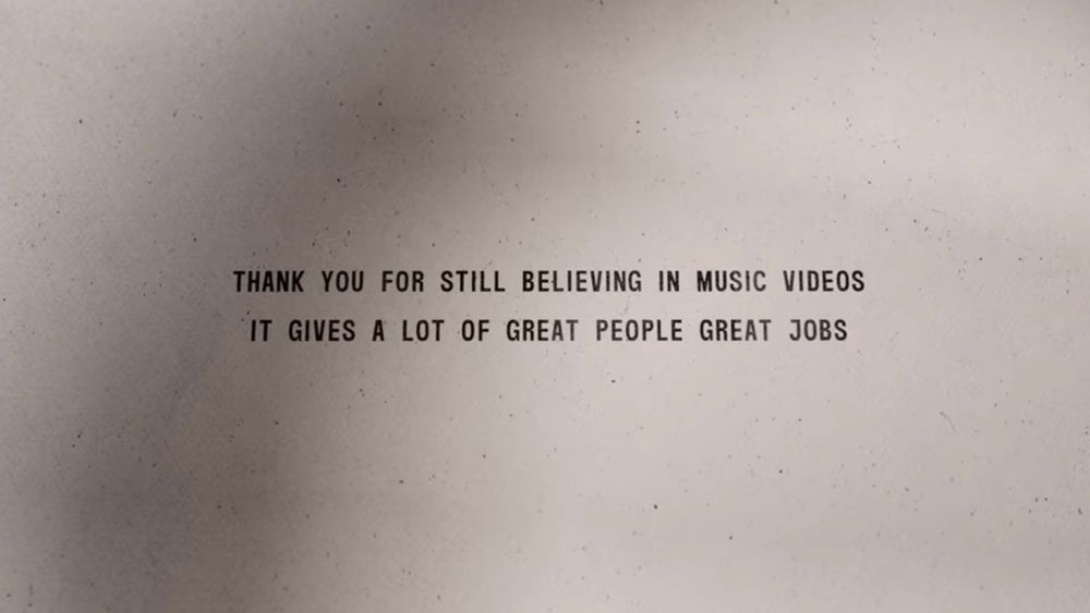 A screenshot from the end of the City Walls music video by Twenty One Pilots. It reads ”Thank you for still believing in music videos. It gives a lot of great people great jobs.” in black all-caps font on a beige paper-like background.