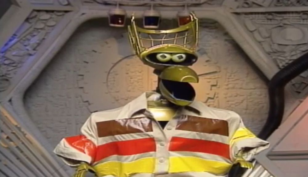 Crow T. Robot in a screen shot from MST3K "Teenagers From Outer Space" where he's in a snappy brown and orange striped 1970s retro shirt.