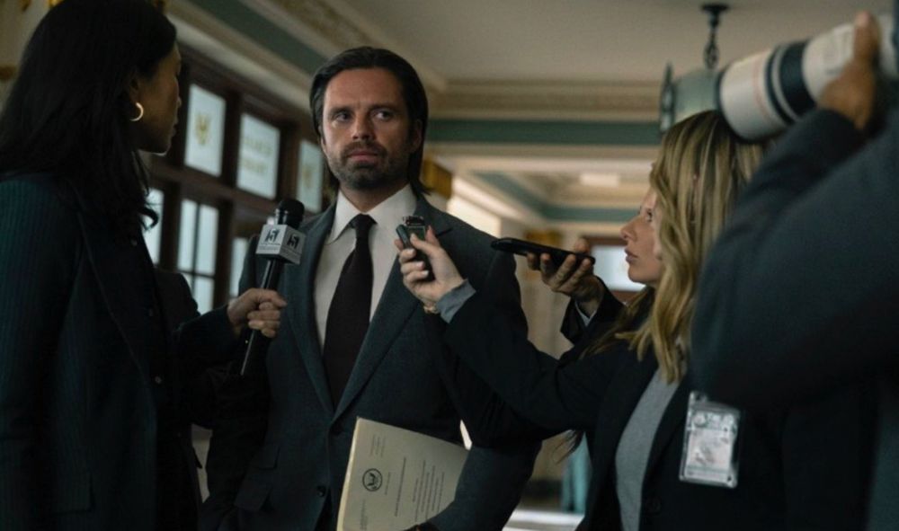 Sebastian Stan as Congressman Bucky Barnes in the movie Thunderbolts*

Barnes is wearing a suit, his hair slicked back, carrying an official case file, as he's stopped in a congressional hallway by media who are holding microphones near his face for a comment. 