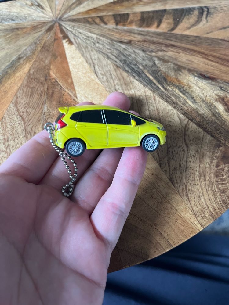 Holding a bright yellow hot wheels Honda Fit on the tips of my fingers