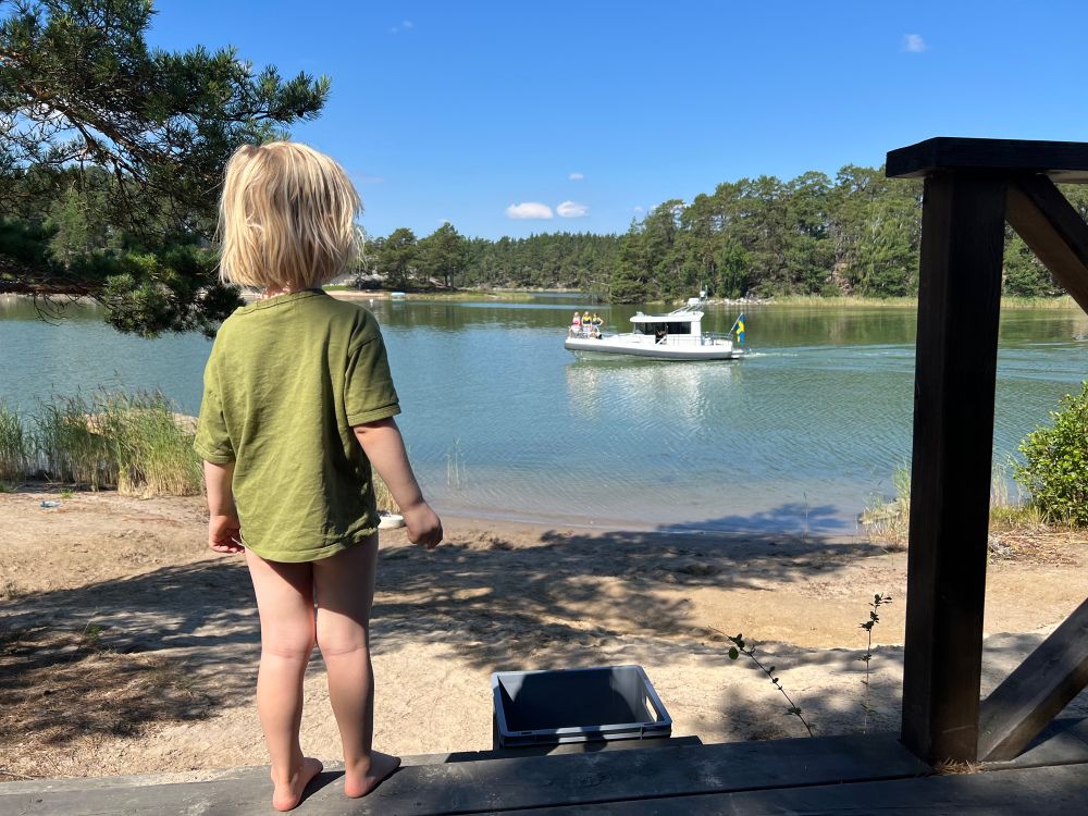 A boy looks at a boat in the water with the island in the distance 