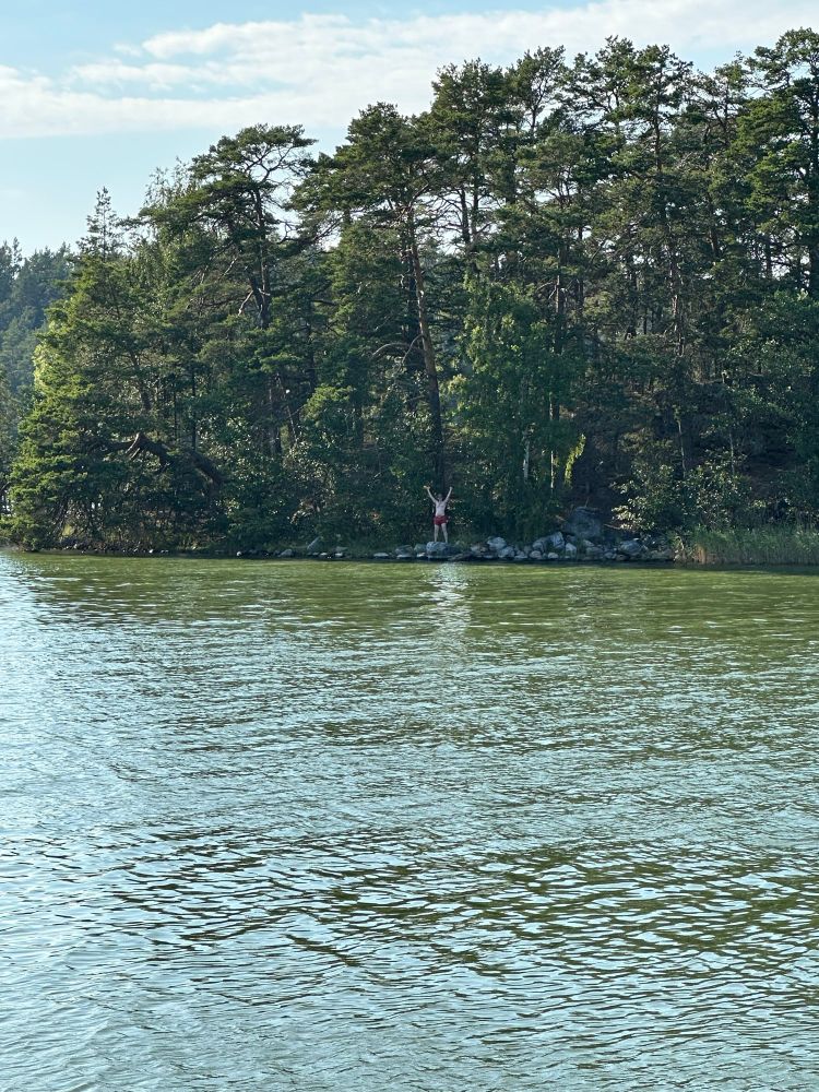 Me standing on a rock on a distant island, raising my arms in triumph with the water I just swam across in the foreground 