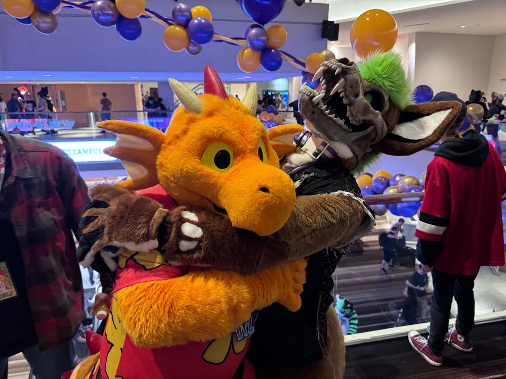 Orange and Red Dragon Fursuit getting hugged by a Skull faced canine creature with green hair