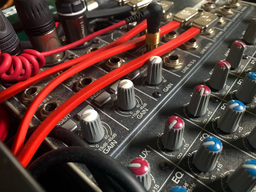 Close-up of a compact audio mixer and Tascam recorder, with bright red quarter-inch cables plugged into LINE IN ports. Knobs, inserts, and balanced XLR outputs are visible, creating a tangle of vibrant connectivity.