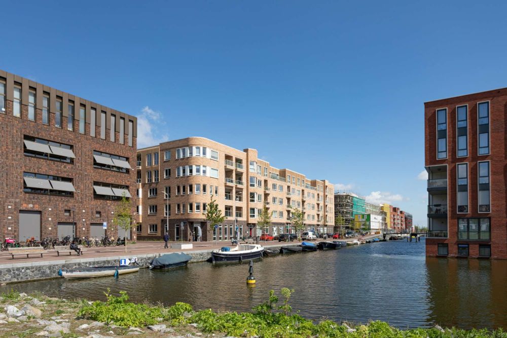 Numerous residential, waterfront buildings along a shared street fronting canals in the Houthavens, Amsterdam