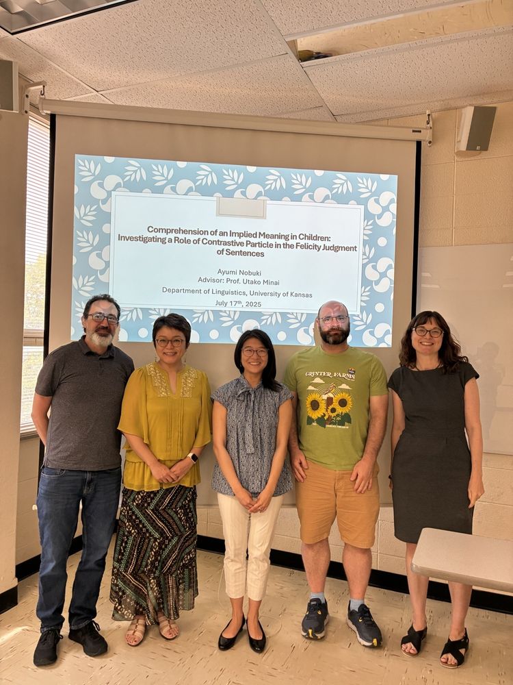 Dr. Ayumi Nobuki standing with her dissertation committee in front of a projector screen from her defense (pictured left to right: Rob Fiorentino, Utako Minai, Ayumi Nobuki, Steve Politzer-Ahles, Alison Gabriele).