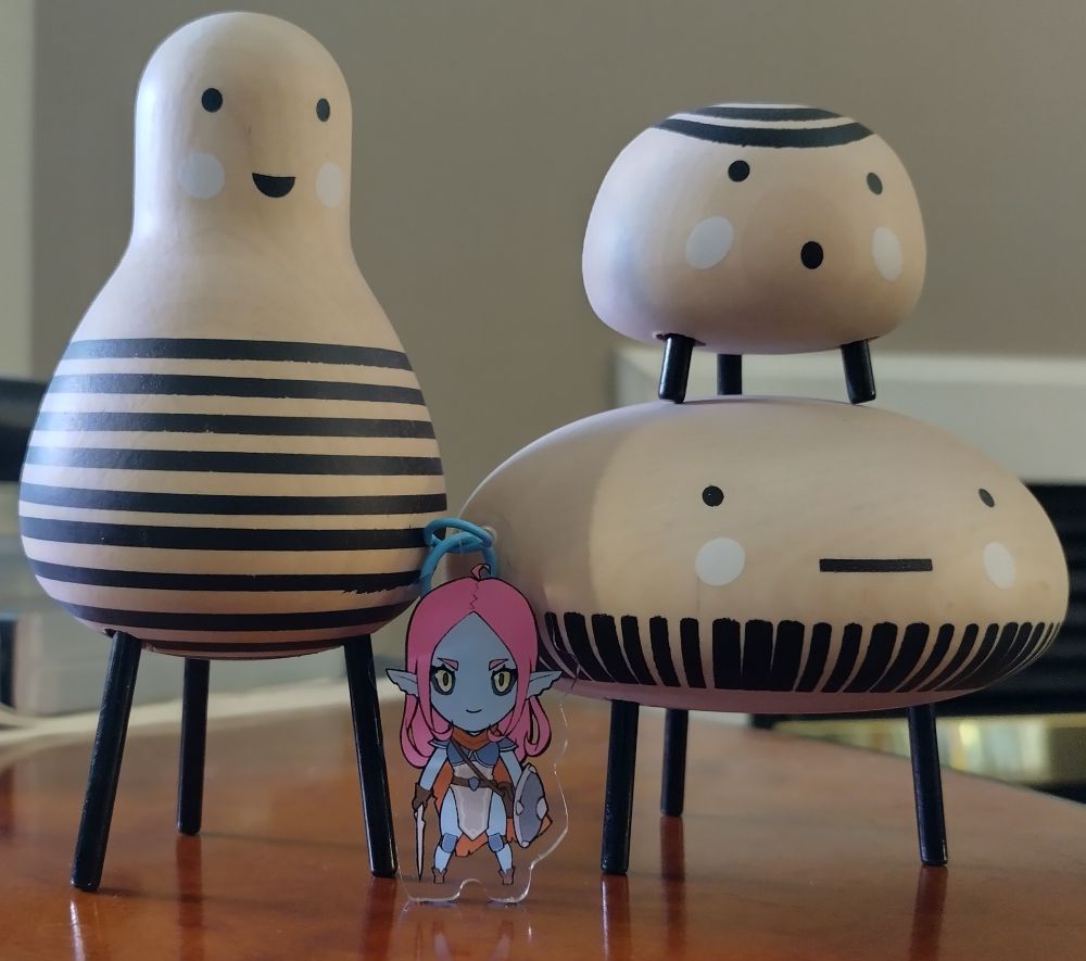 An acrylic keychain of Mariah Doeheart from the BREAK!! tabletop rpg standing alongside some very odd but charming little creature sculptures