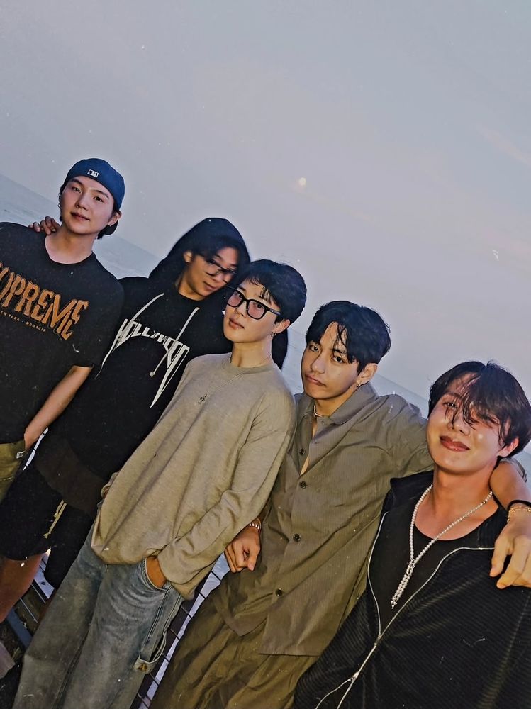FIVE MEMBERS OF BTS!!!! AFTER DINNER IN LOS ANGELES ON A BALCONY OVERLOOKING THE WATER. J-HOPE looking blushy and lightly toasted on a charcoal zip up and pearls. V looking goofy in a taupe matching set. Jimin posing skeptically(?) in a gray long-sleeved tee and jeans. RM in motion, looking behind the group, in a black hoodie and shorts. SUGA looking STUNNING in a black graphic tee and blue backwards baseball cap outserving the lot.