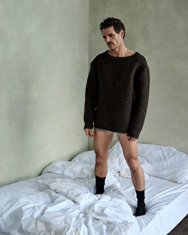 Pedro Pascal in an image from his Vanity Fair shoot. He’s standing on an unmade bed, wearing a dark sweater that’s just a little too big, so the sleeves nearly hide his hands, and the hem nearly hides gray boxer-briefs (I think? I think about too much), and ankle-length black socks which really should not be sexy. Send help.