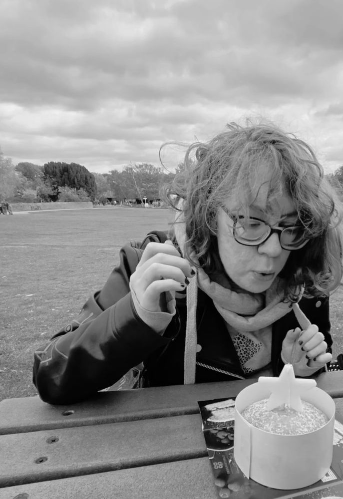 Black and white photo of a windswept woman, aged 35 years and 364 days, blowing out a candle on an m&s Victoria sponge. She promises she has friends with her to help her eat the cake.