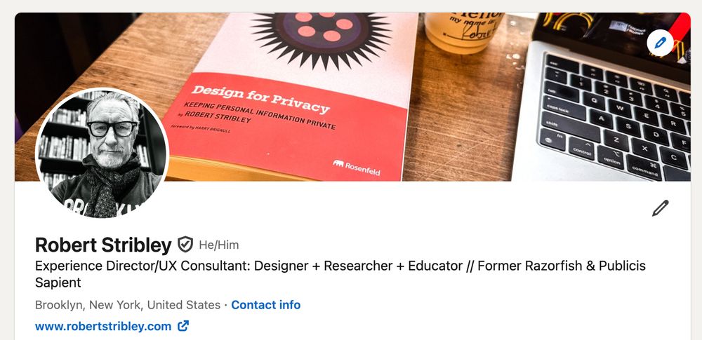 Photo of LinkedIn header for the poster with the book "Design by Privacy" by the poster in the image, plus a cappuccino in a paper cup with the name "Robert" written on it, plus an open laptop, all sitting on a cafe counter.