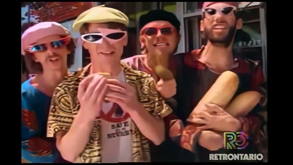 Screenshot from the Retrontario YouTube channel's "Spadina Bus" video showing four men dressed in stereotypical beatnik outfits, variously wearing crazy sunglasses, long goatees, and berets. The second man is wearing a T-shirt reading "Save the stubby" [a uniquely Canadian beer bottle shape]. The tallest man, on the right, is holding two loaves of bread.
