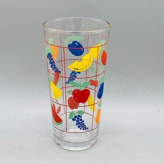 A tall drinking glass with a painted on grid is various colorful fruits