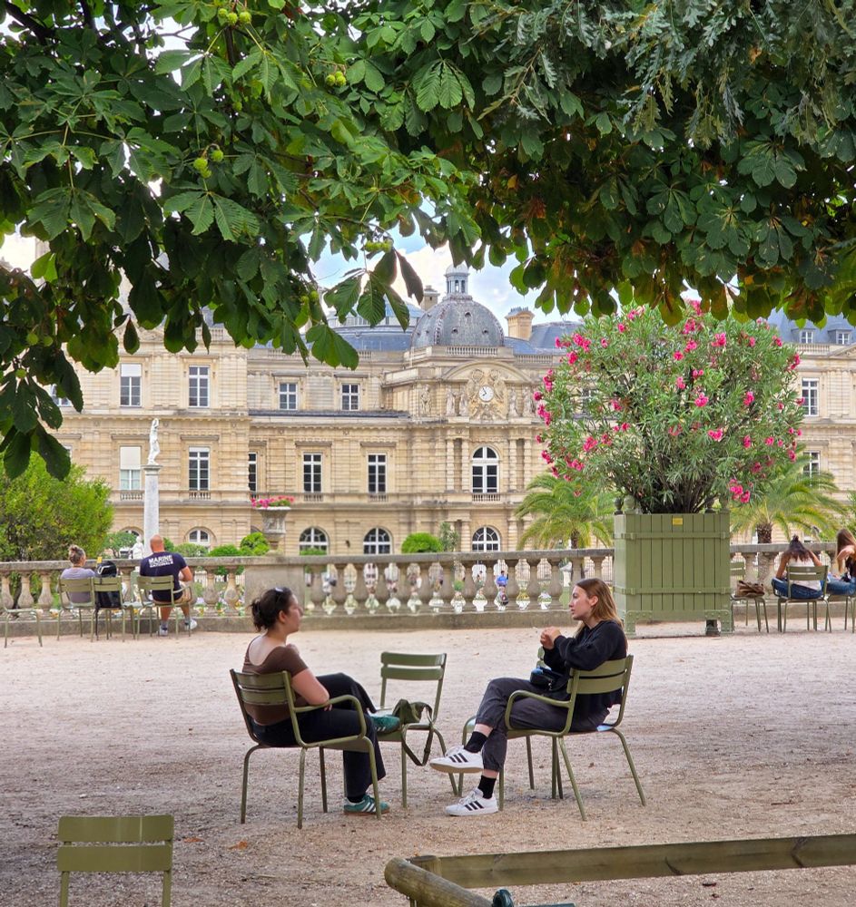 En arrière plan le Palais du Luxembourg, 2 femmes discute sur les chaises au premier plan 