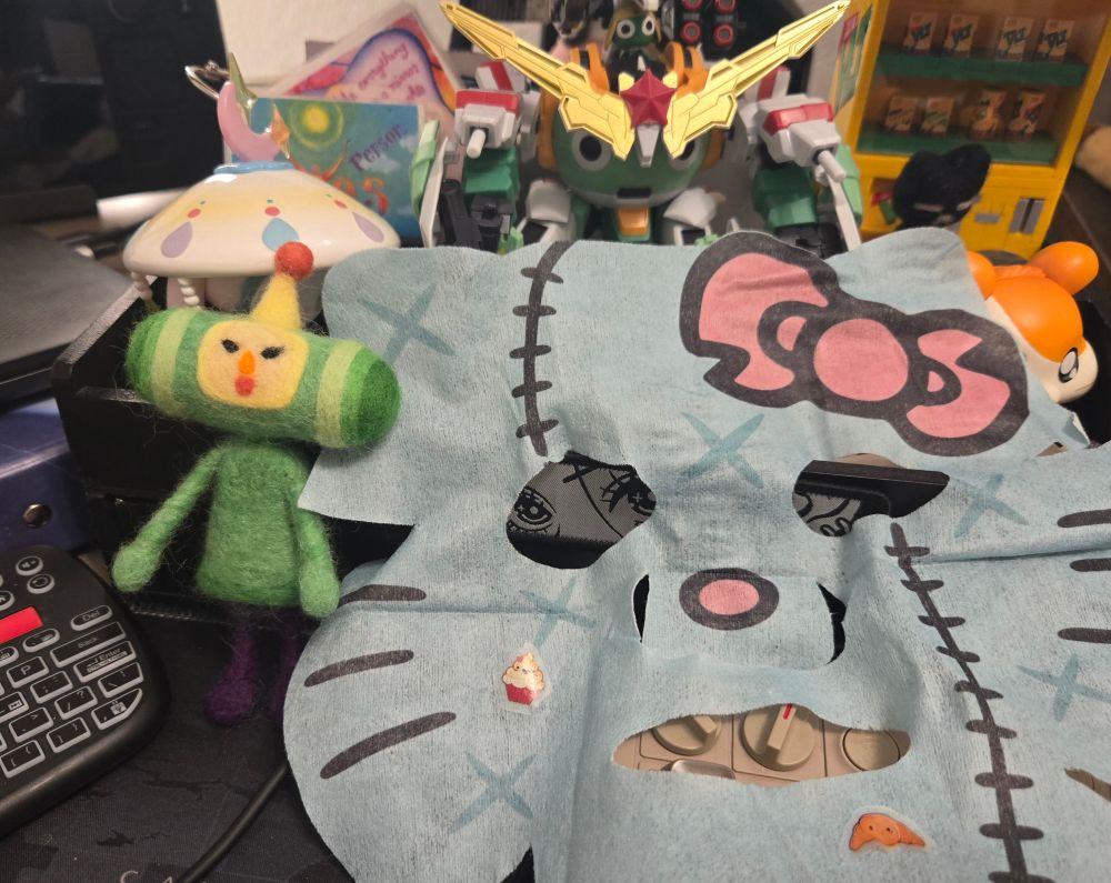 Close up on the Zombie Hello Kitty Face Mask and The Prince Katamari I needle felted surrounded by various trinkets on my desk!