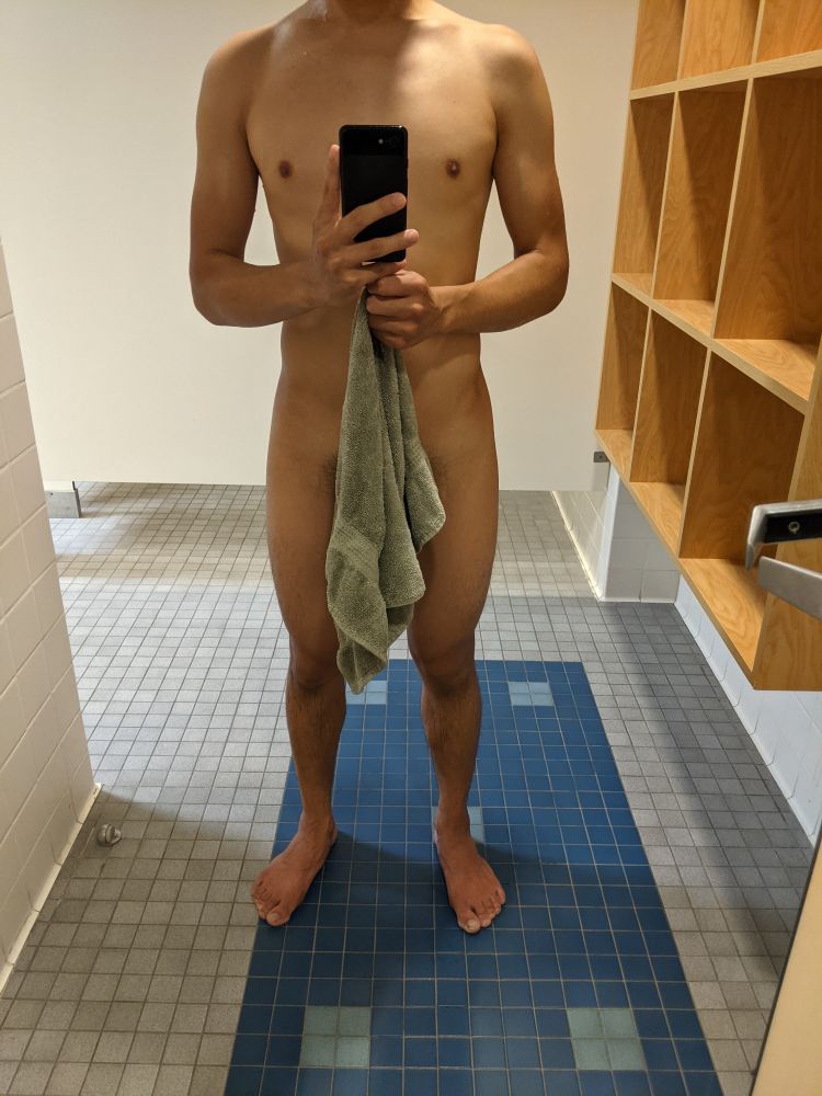 Guy standing in front of a mirror, naked except for a hand towel held in front of him. 