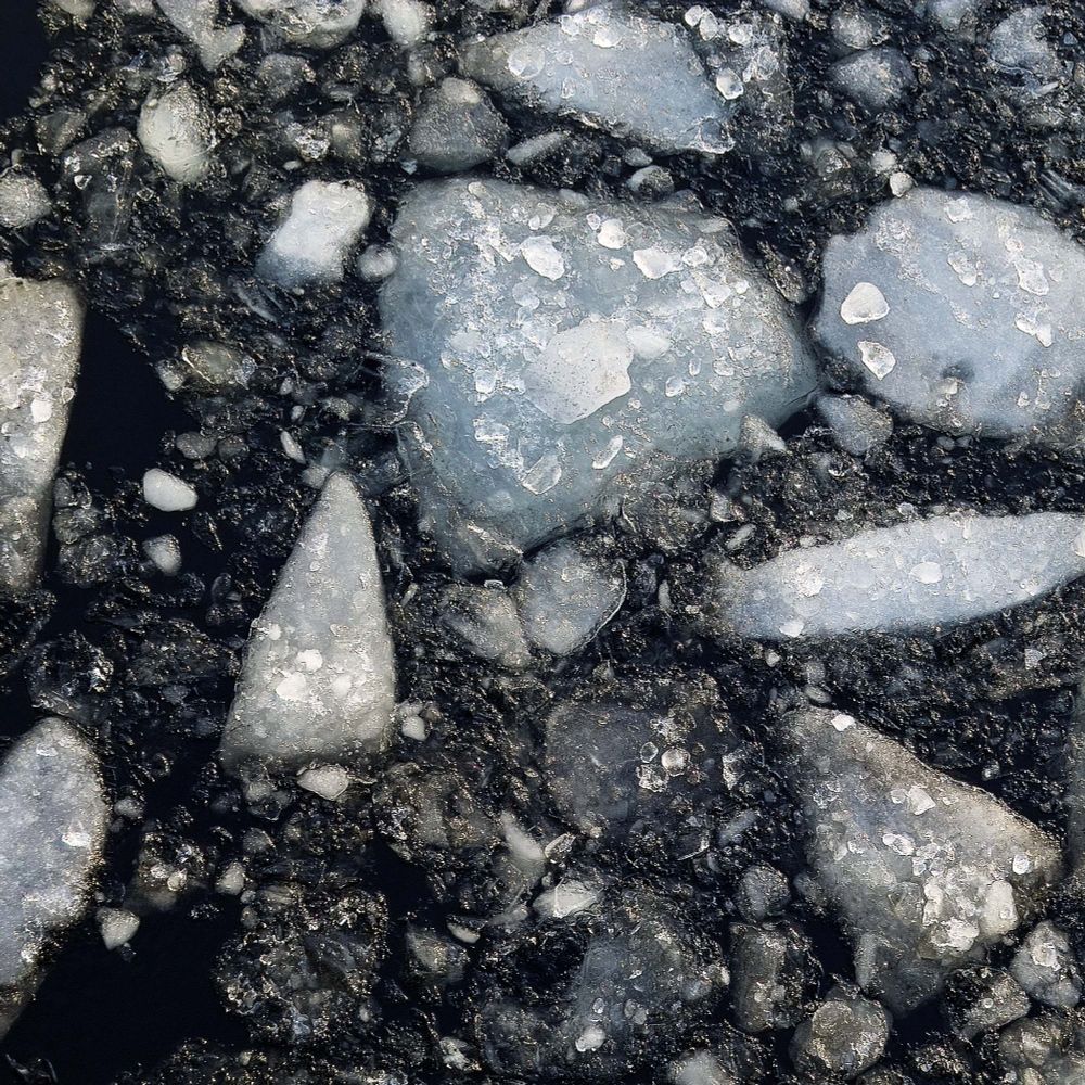 View from above of a river in winter. Large, smaller and very small pieces of ice float in the darkness of the river. They are white, yellowish or brownish, with slightly rounded corners. They come in different shapes, from triangular to round.
