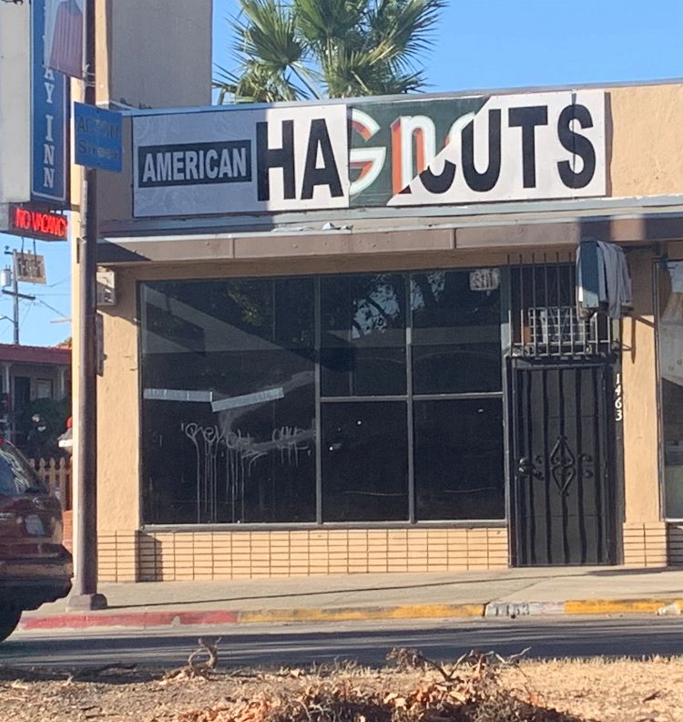 a store on a street corner. the stores sign is partially torn revealing part of an older sign underneath. the sign now (arguably) reads 'american hagnuts'