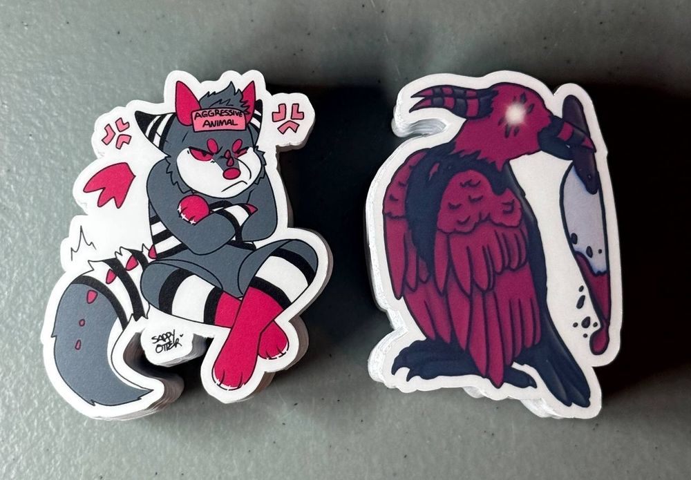 A stack of angry demon dog stickers and also murder-y horned crow stickers.