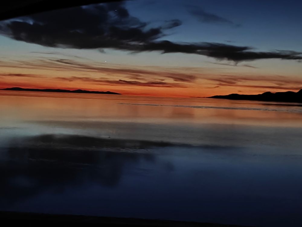 Some dark evening clouds with red in the distance and a calm lake underneath 