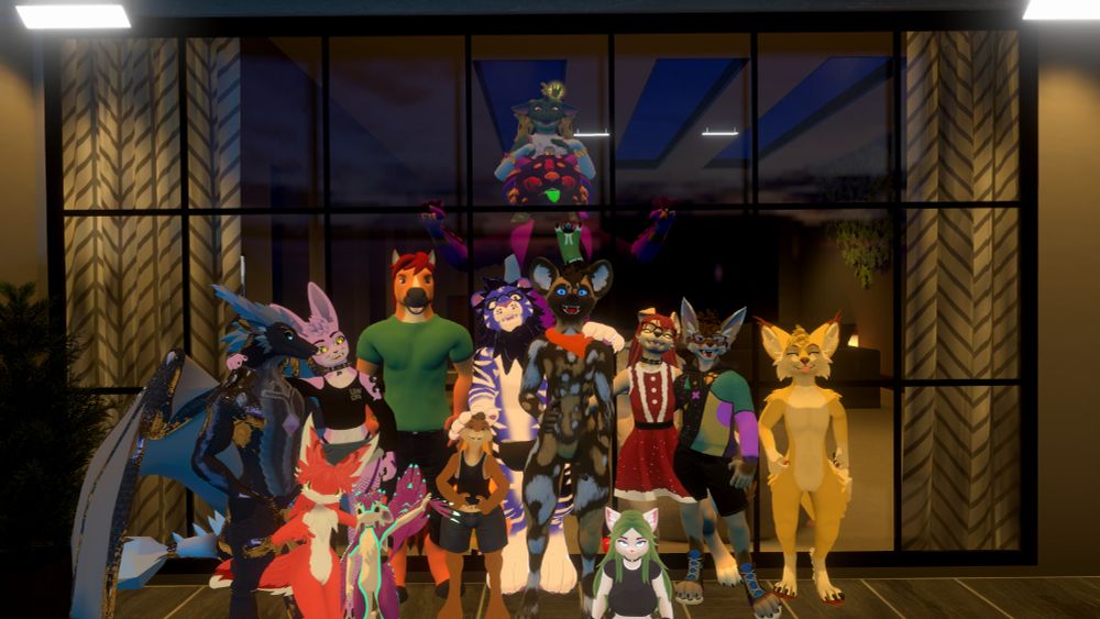 A large collection of VRChat players posing for a group photo. Several characters are visible, each varying in species, colors, fur/scale/hair patterns, etc. The majority of the characters are displaying happy, excited or confident expressions and are embracing each other.