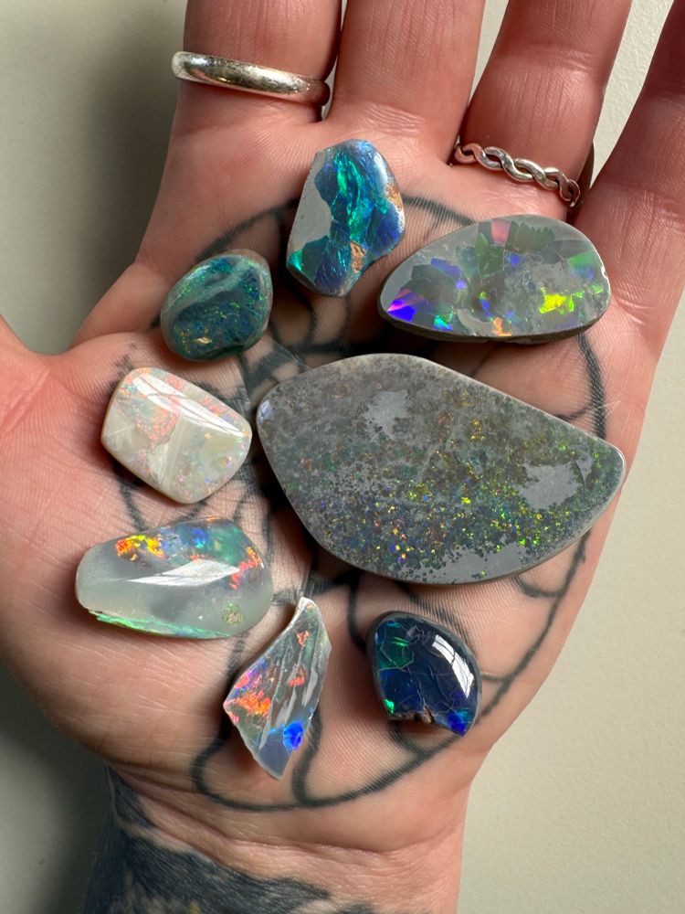 Photo of a hand palm side up holding a selection of opal cabs from Australia which shows vibrant flashes of colour, ranging from green to blue, pink, yellow, peach and orange. Held in collections of The Hunterian, University of Glasgow. Head Like A Hole (Opal) is the name of a Nine Inch Nails remix version of HLAH, included on the uk version of the album.