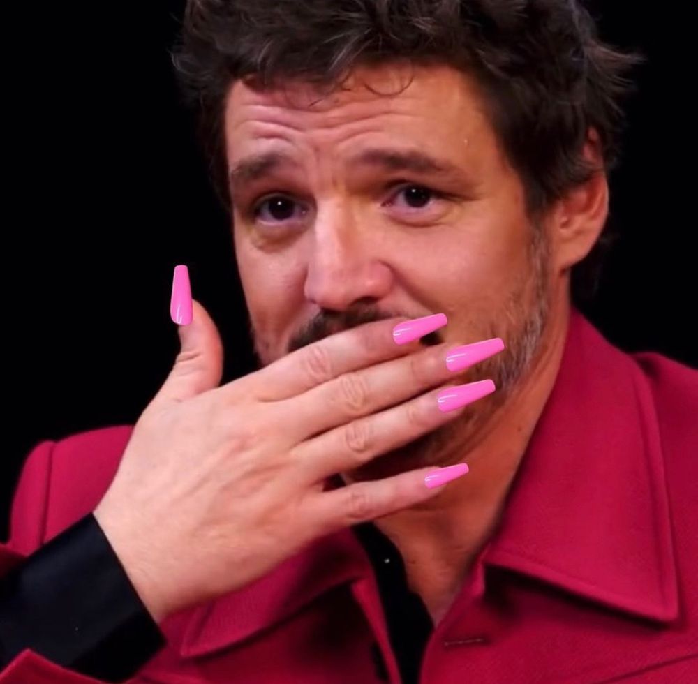 Still taken from the Hot Ones episode with Pedro pascal in a red jacket, photoshopped to look like he’s covering his own mouth with one hand that has long pink acrylic nails 