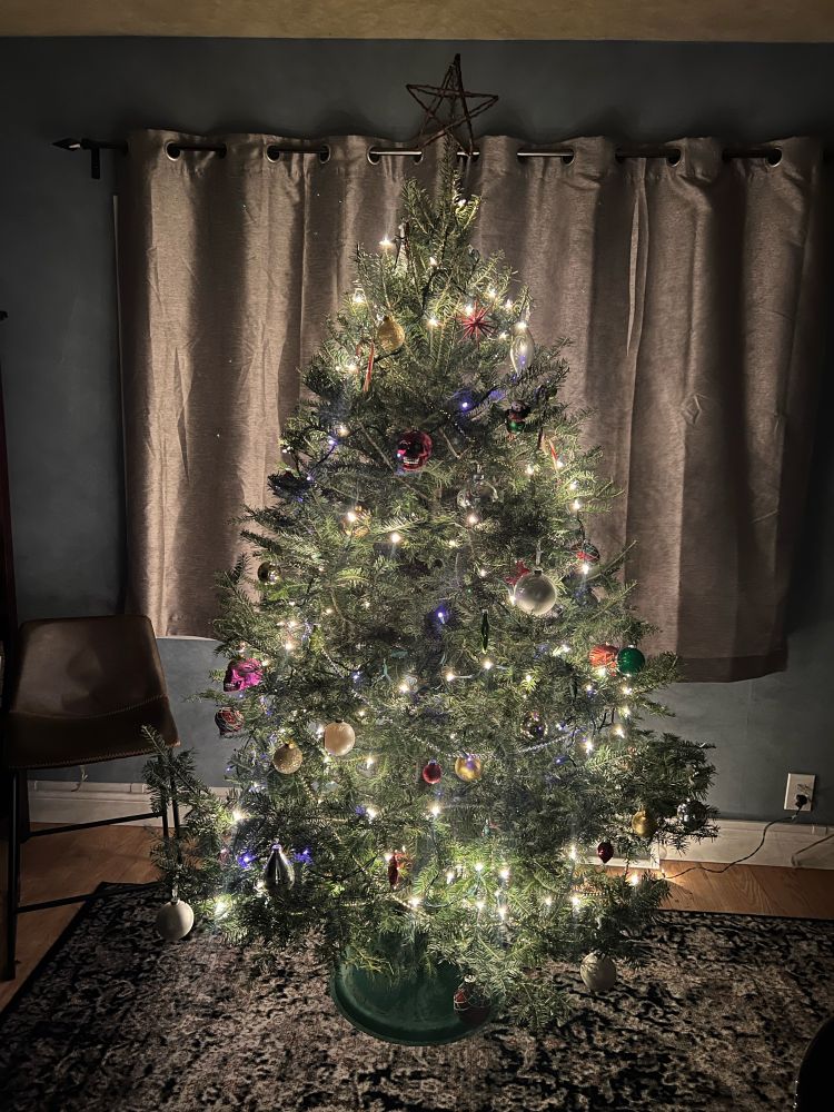 A decorated Christmas tree set in front of closed curtains in a room with blue walls and an area rug