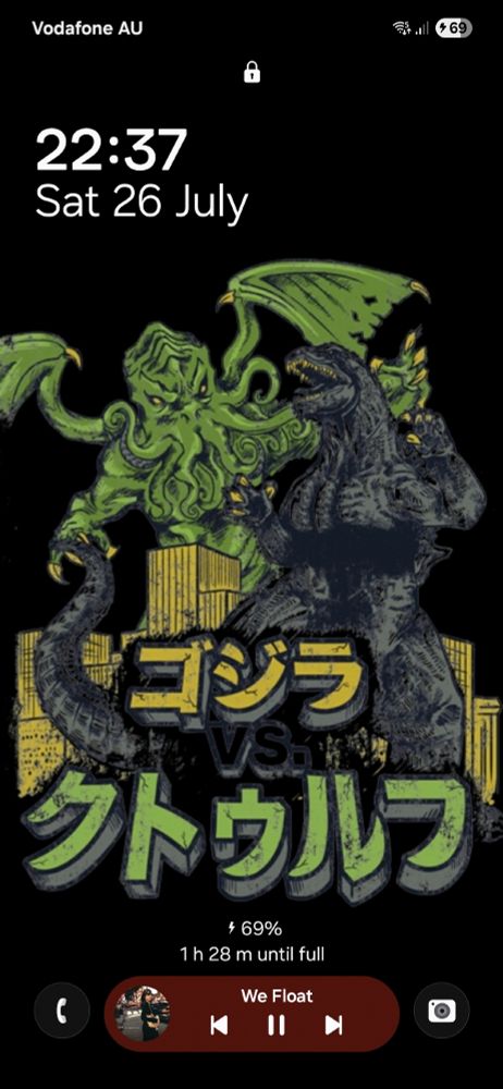 A lockscreen with a graphic of Godzilla and Cthulhu fighting in front of a cityscape, battery at 69% (lol), and We Float by PJ Harvey currently playing.