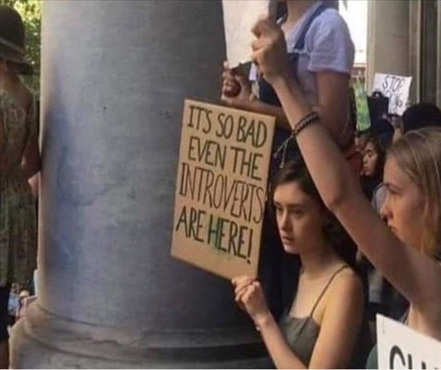 A girl protesting holding a sign that says “it’s so bad even the introverts are here!”